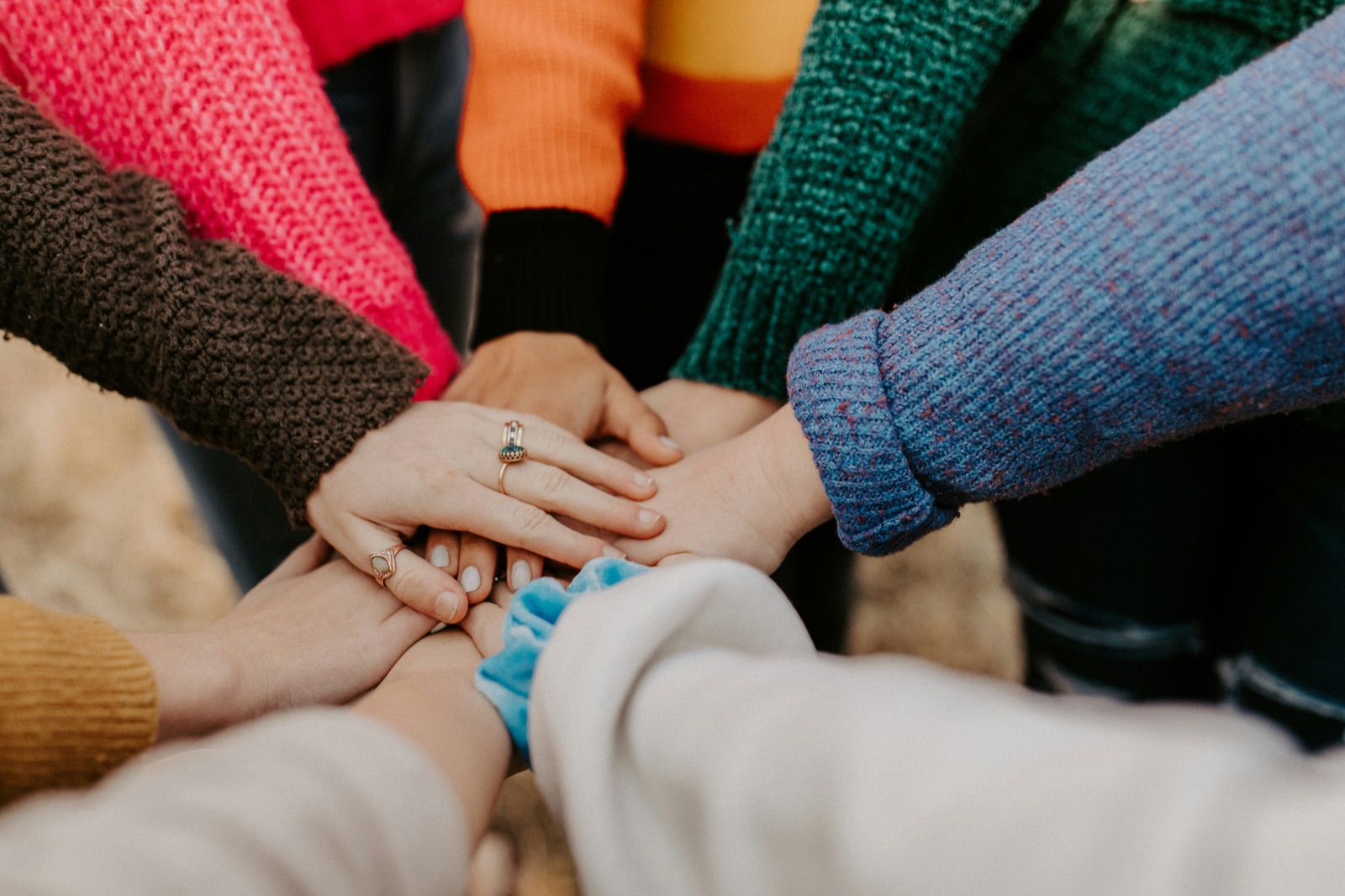 A circle of people in colorful sweaters stacking their hands together